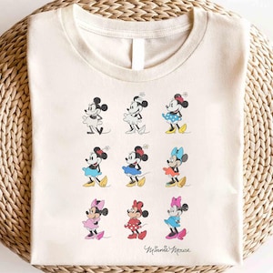 May include: A beige t-shirt with a graphic print of nine different Minnie Mouse characters in various poses and outfits. The text "Minnie Mouse" is printed at the bottom of the shirt.