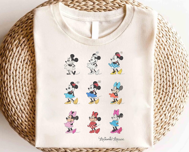 May include: A beige t-shirt with a graphic print of nine different Minnie Mouse characters in various poses and outfits. The text "Minnie Mouse" is printed at the bottom of the shirt.