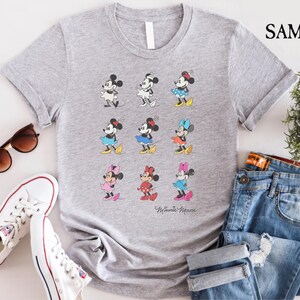 May include: Gray t-shirt with a graphic of nine different Minnie Mouse characters in various poses and colors. The text "Minnie Mouse" is printed at the bottom of the shirt.