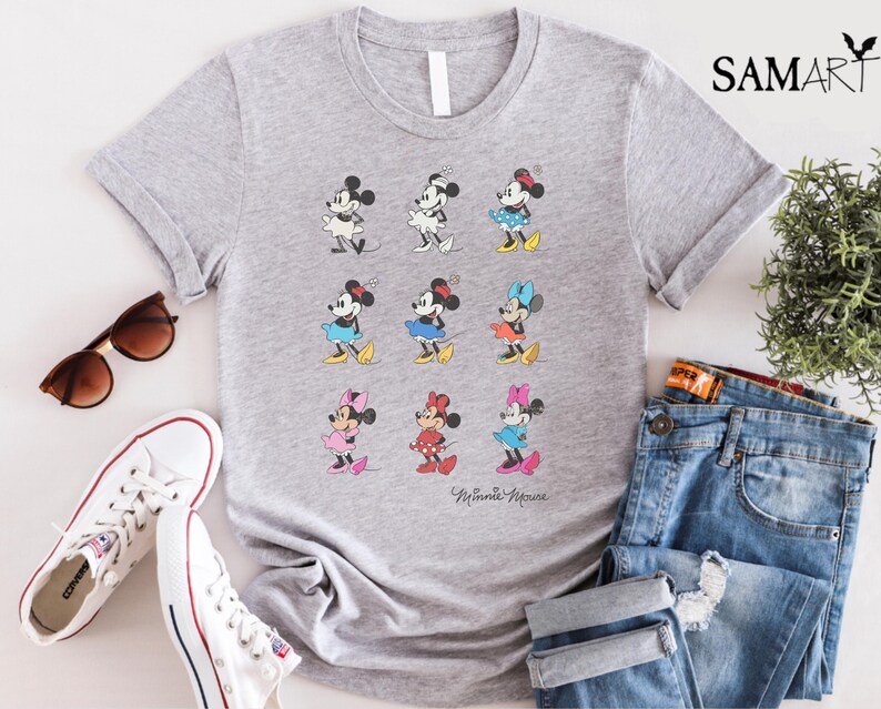 May include: Gray t-shirt with a graphic of nine different Minnie Mouse characters in various poses and colors. The text "Minnie Mouse" is printed at the bottom of the shirt.