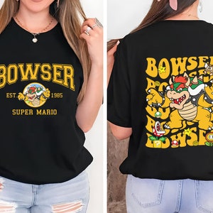 May include: Black t-shirt with a yellow and red Bowser graphic and the text "BOWSER EST. 1985 SUPER MARIO" on the front. The back of the shirt features a larger Bowser graphic with the text "BOWSER" in a yellow and red font.