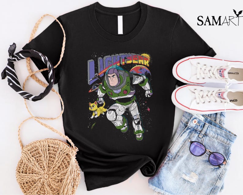 May include: Black t-shirt featuring a graphic of Buzz Lightyear from the Toy Story franchise. The graphic depicts Buzz in his space ranger suit with a yellow cat in the background. The text "LIGHTYEAR" is printed above Buzz.