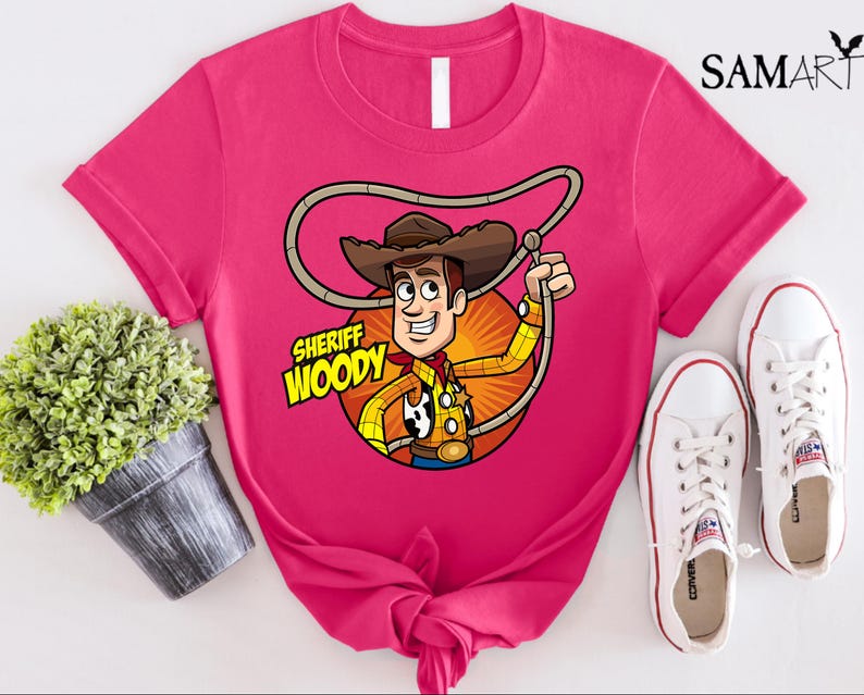 Pode incluir: Camiseta rosa com uma imagem de desenho animado do Woody do Toy Story. A imagem mostra o Woody usando seu distintivo de xerife e seu chap&eacute;u. O texto "Sheriff Woody" est&aacute; impresso na camiseta.