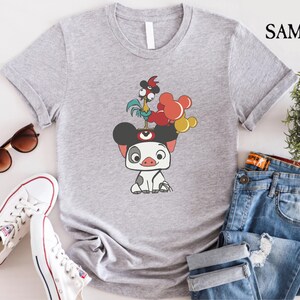May include: A light gray t-shirt featuring a cartoon illustration of a pig with mouse ears, a rooster, and balloons. The shirt is paired with blue jeans, white sneakers, and sunglasses.
