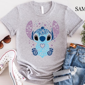 May include: A gray t-shirt with a blue and purple Stitch character design. Stitch is surrounded by hearts and flowers.