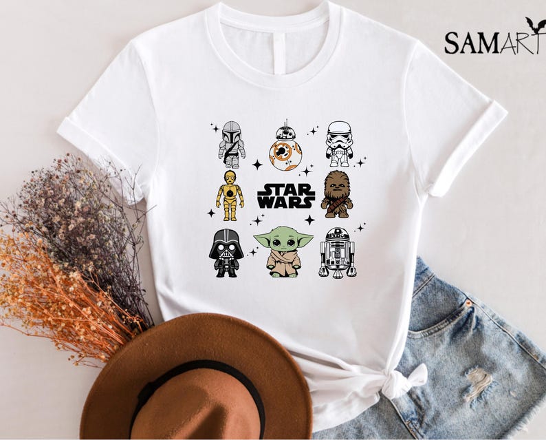 K&ouml;nnte beinhalten: Wei&szlig;es T-Shirt mit einem Star Wars-Design, das Cartoon-Charaktere wie Darth Vader, Yoda und R2-D2 zeigt. Der Text "STAR WARS" ist ebenfalls zu sehen. Das T-Shirt wird mit einem braunen Hut und Jeansshorts pr&auml;sentiert.