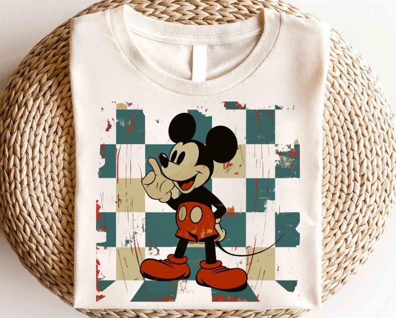 May include: A white t-shirt with a vintage-style graphic of Mickey Mouse on a checkered background. The graphic has a distressed look with faded colors and a worn texture.