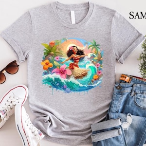 Pode incluir: Uma camiseta cinza claro com uma ilustra&ccedil;&atilde;o colorida de uma mulher em um cen&aacute;rio tropical. O design inclui uma mulher com um top vermelho e uma saia bege, cercada por flores, ondas e palmeiras. &Oacute;culos de sol, t&ecirc;nis brancos e jeans tamb&eacute;m s&atilde;o vis&iacute;veis.
