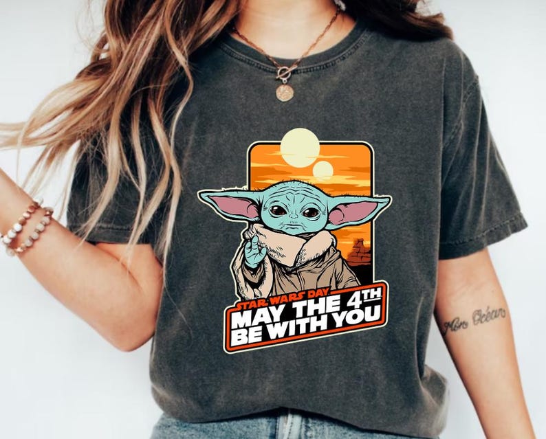 May include: A dark gray t-shirt with a graphic of a baby Yoda character from Star Wars. The graphic includes the text "Star Wars Day May the 4th Be With You".