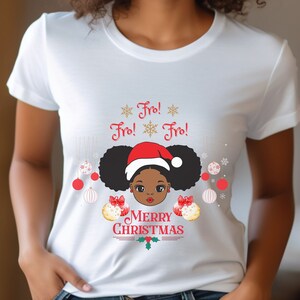 May include: White t-shirt with a Christmas design featuring a cartoon Black girl with afro puffs wearing a Santa hat. The design includes the text "Fro! Fro! Fro!" and "Merry Christmas" with gold snowflakes and ornaments.