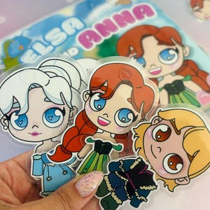 Puede incluir: Cuatro pegatinas de personajes de dibujos animados coloridos con Elsa, Anna y otros dos personajes de la pel&iacute;cula Frozen. Las pegatinas est&aacute;n sobre un fondo transparente y tienen un acabado brillante.