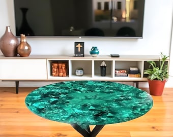 May include: Round coffee table with a vibrant teal and black epoxy resin top. The table has a black metal base with a unique, angled leg design. The table's top has a glossy finish and is set on a wooden floor.