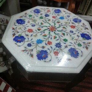 May include: Octagonal white marble table top with a floral design inlaid with colorful stones. The table top is surrounded by a dark wood frame.