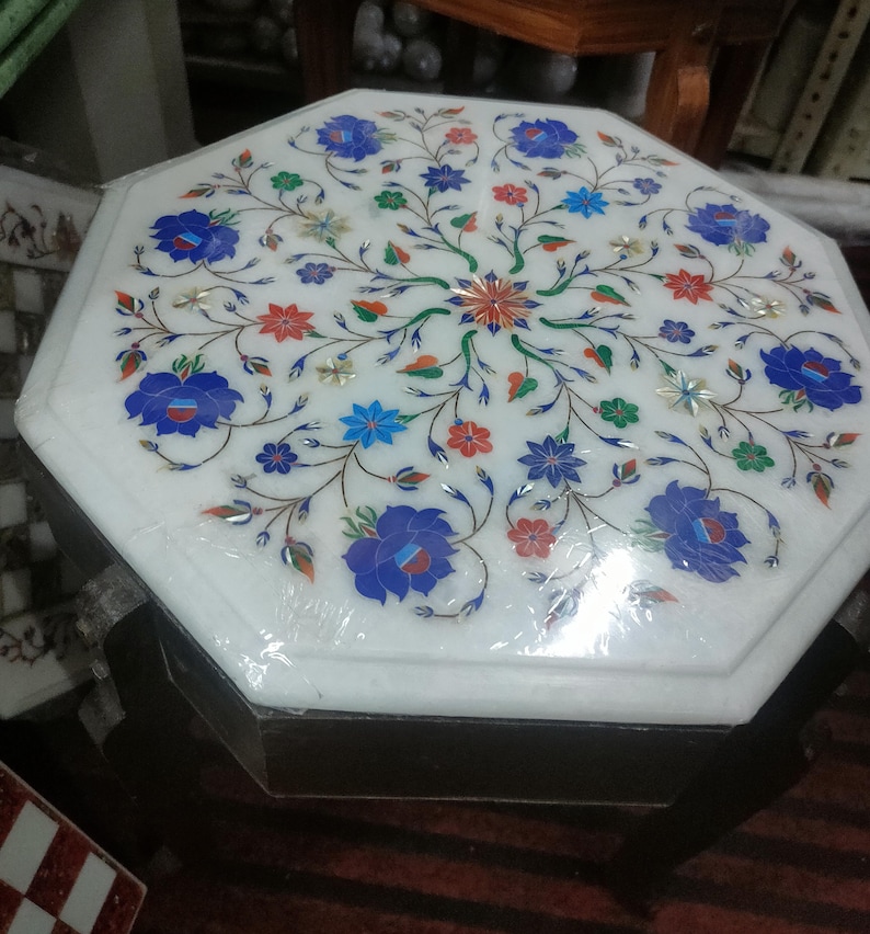 May include: Octagonal white marble table top with a floral design inlaid with colorful stones. The table top is surrounded by a dark wood frame.