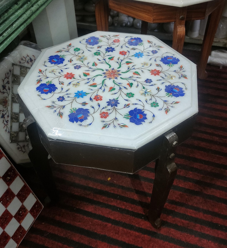 May include: Octagonal white marble table with intricate floral inlay in blue, red, green, and gold. The table has a dark wood base with four legs.