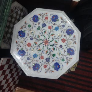 May include: Octagonal white marble table top with intricate floral design inlaid with colorful stones. The design features blue, red, green, and gold accents.
