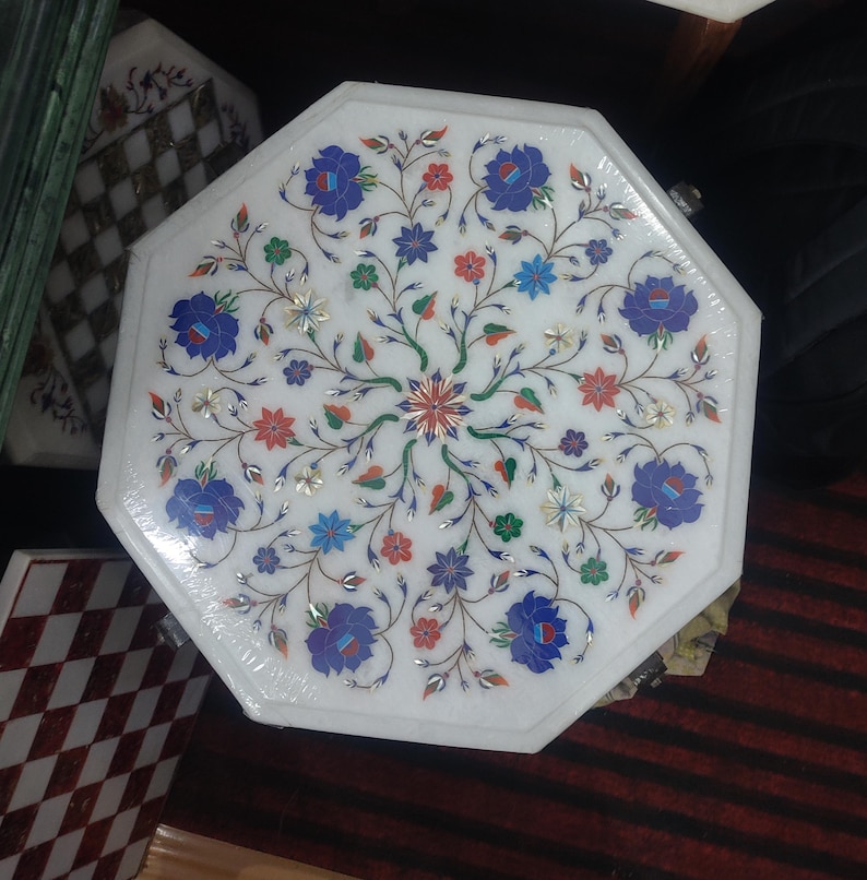 May include: Octagonal white marble table top with intricate floral design inlaid with colorful stones. The design features blue, red, green, and gold accents.