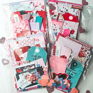 May include: Four clear cellophane bags filled with Valentine's Day themed paper ephemera. Each bag contains tags, cards, and decorative elements in shades of red, pink, and white. Some tags read "Time", "Love Letters", and "I Like You A Bot".