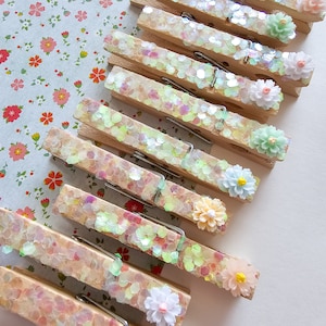 May include: A set of wooden clothespins decorated with iridescent glitter and pastel-colored flowers. The clothespins are perfect for adding a touch of whimsy to your home decor.