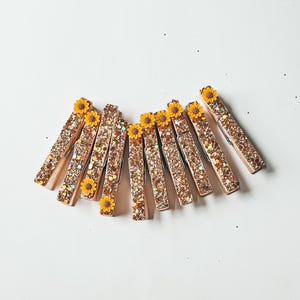 May include: Ten gold glitter clothespins with yellow sunflower embellishments.
