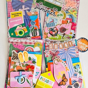 May include: Four colorful scrapbook kits with summer-themed embellishments. Each kit includes decorative paper, stickers, and die-cuts featuring travel motifs like cameras, passports, and a green van. The word "summer" is visible on one kit.