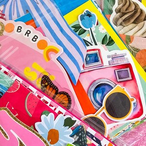 May include: A collection of colorful stickers and decorative paper items. The image features a pink camera, sunglasses, a butterfly, and the text "BRB". Other designs include a blue bow, flowers, and fruit.