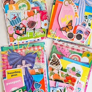 May include: Four colorful, decorative paper packs filled with travel-themed ephemera. Each pack features a variety of stickers, tags, and paper cutouts with images of cameras, butterflies, and cocktails. The packs are sealed in clear plastic.