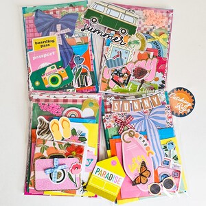 May include: Four clear plastic pouches filled with colorful travel-themed ephemera. Each pouch contains decorative paper, stickers, and die-cuts with summer and vacation motifs, including cameras, passports, and a green camper van.