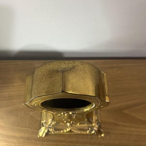 May include: A gold-toned mantel clock with an ornate base and a round face. The clock is made of metal and has a decorative design.