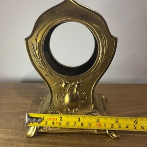 May include: A gold-coloured metal stand with an ornate design and a round opening in the centre. The stand is approximately 10 inches wide.