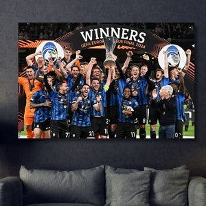 Può includere: Un gruppo di calciatori in uniforme blu e bianca che tiene in alto un trofeo. Il trofeo è d'argento e ha una base blu. I giocatori sorridono e festeggiano la loro vittoria. Il testo "WINNERS UEFA EUROPA LEAGUE FINAL 2024" è visibile nella parte superiore dell'immagine.