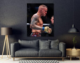 May include: A rectangular wall art print featuring a side profile of a mixed martial arts fighter with a nose injury, wearing gold UFC gloves and patterned fight shorts, displayed in a living room setting above a grey sofa and wooden side table.