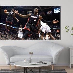 May include: A rectangular wall art print featuring a dynamic basketball game scene. The image captures two players in black Miami Heat uniforms, one with number 3 and one with number 6, competing on a court with a crowd and arena lights visible.