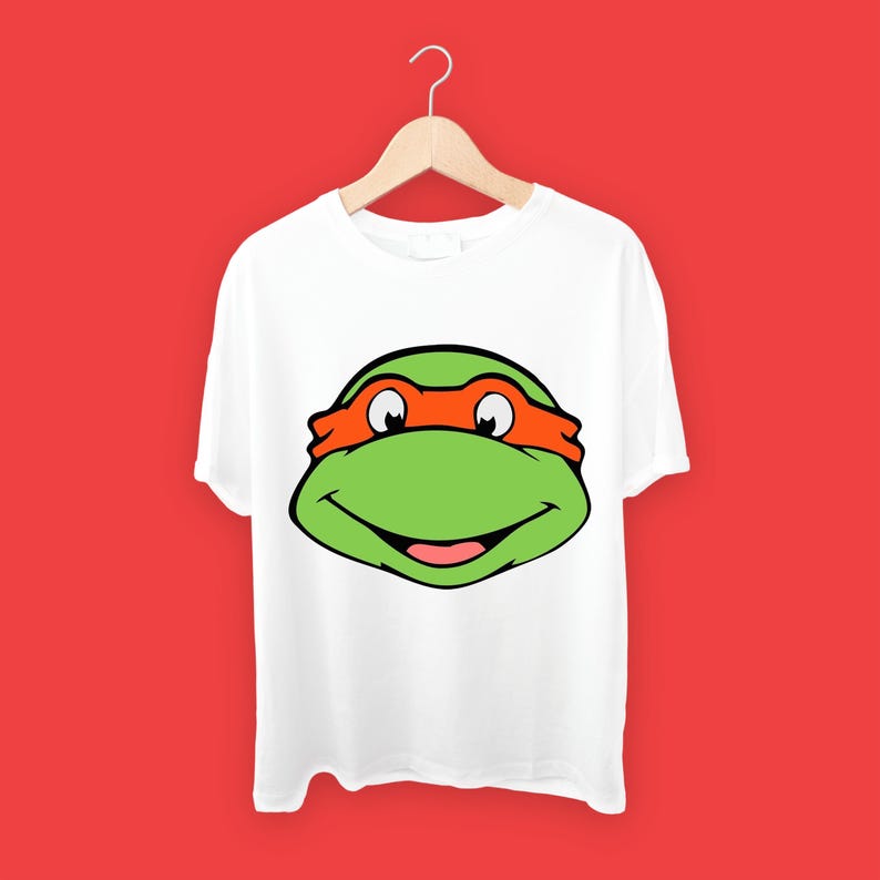 May include: White t-shirt with a green and orange Teenage Mutant Ninja Turtles character face graphic.