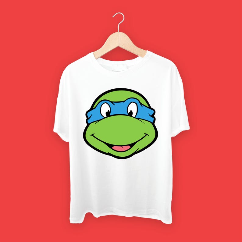 May include: White t-shirt with a green and blue cartoon turtle head graphic. The turtle is wearing a blue mask and has a big smile.