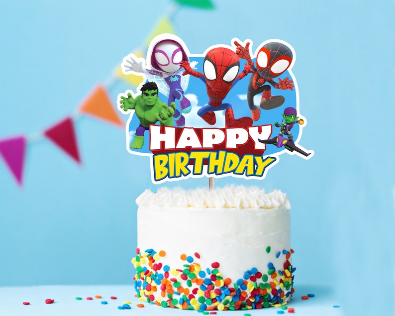 May include: A white cake with colorful sprinkles and a cake topper featuring Spider-Man, Spider-Gwen, Hulk, and Green Goblin characters. The topper says "Happy Birthday".