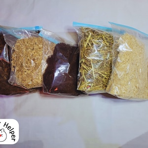 May include: Five clear plastic bags filled with different types of bedding for small pets, such as hamsters. The bedding includes brown wood shavings, brown shredded paper, brown and black coffee grounds, brown hay, and white wood shavings.