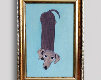 May include: A framed painting featuring a brown dachshund viewed from above against a light blue background. The dog has a long body and a tan head with dark eyes. The artwork is enclosed in an ornate, metallic gold frame with a textured edge.