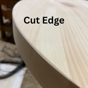 May include: Close-up of a light-coloured wooden table with a rounded edge. The text "Cut Edge" is printed in black on the surface. The wood grain is visible, and the edge appears freshly cut.