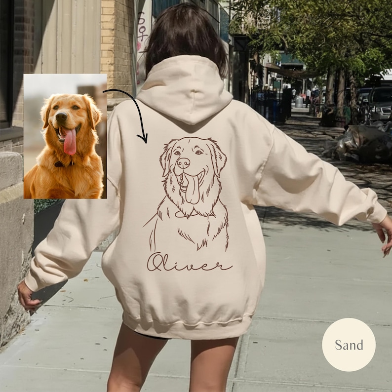 May include: A sand-coloured hoodie with a line drawing of a Golden Retriever on the back, tongue out, and the name "Oliver" underneath. A smaller photo of the dog is on the left. The hoodie has a hood.