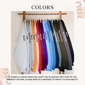 May include: A selection of sweatshirts in a variety of colours, including white, grey, pink, red, blue, and black, displayed on a wooden rack. The image includes the word "COLORS" at the top.