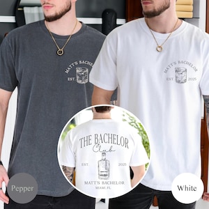 May include: Two short-sleeved t-shirts, one pepper-colored and one white, featuring a graphic of a cocktail glass and the text "MATT'S BACHELOR EST. 2025". The back of the white shirt displays "THE BACHELOR CLUB" and "MATT'S BACHELOR MIAMI, FL".