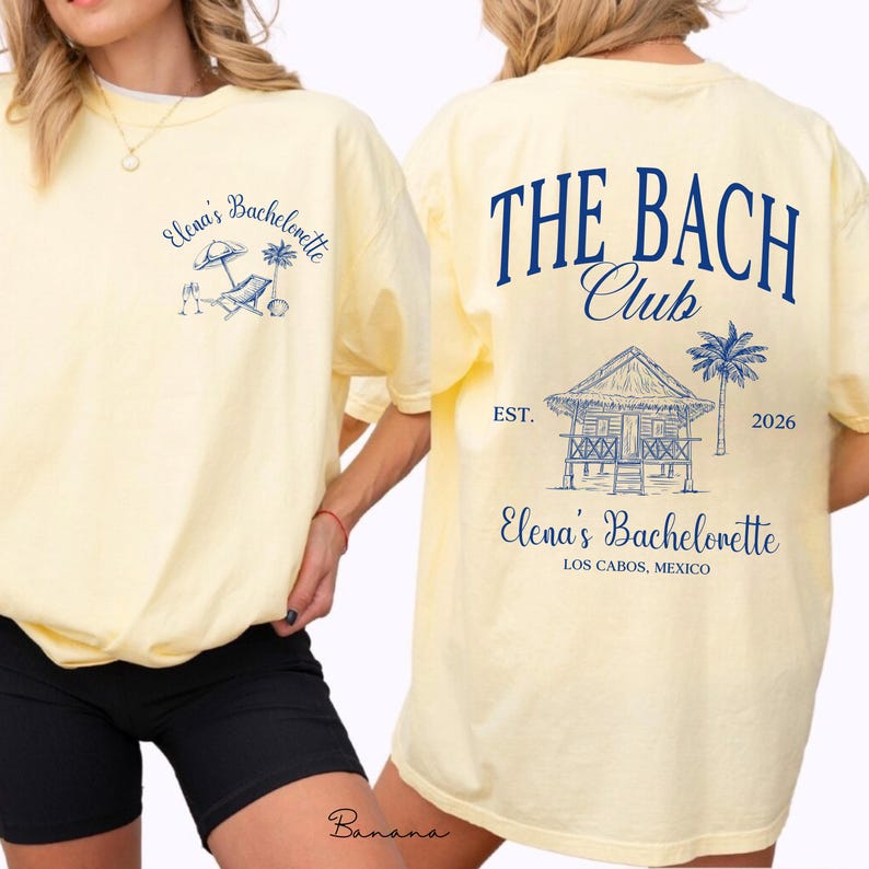 May include: A light yellow t-shirt with navy blue graphics. The front features "Elena's Bachelorette" with beach-themed illustrations. The back displays "THE BACH Club" above a beach hut design, palm tree, and "Elena's Bachelorette, Los Cabos, Mexico."