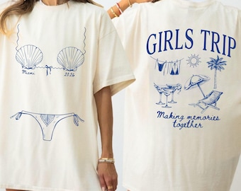 Könnte beinhalten: Cremefarbenes T-Shirt mit blauem Muschel- und Bikini-Design auf der Vorderseite. Auf der Rückseite des Shirts stehen die Worte "GIRLS TRIP" und Strandmotive. Der Satz "Making memories together" ist ebenfalls auf der Rückseite aufgedruckt.