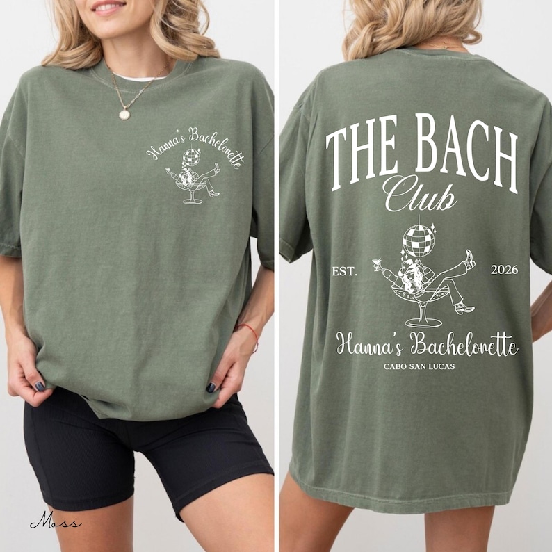 May include: Moss green t-shirt with white text and graphic. The front features "Hanna's Bachelorette" and a graphic of a person in a chair. The back says "THE BACH CLUB" with "EST. 2026" and "Hanna's Bachelorette CABO SAN LUCAS".