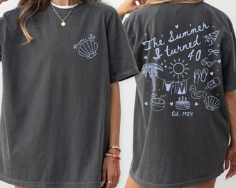 May include: Dark gray t-shirt with a round neck. The front features a seashell graphic and the text "Miami, FL". The back has the text "The Summer I turned 40" with summer-themed illustrations, including a palm tree, sun, and cake. Est. 1985.