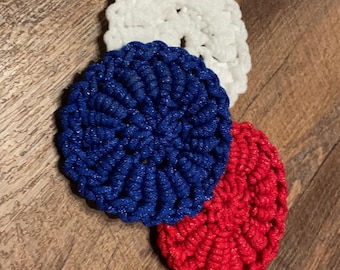 Peut inclure: Trois dessous de verre crochetés aux couleurs patriotiques : blanc, bleu et rouge. Les dessous de verre ronds ont un aspect texturé et tissé. Ils sont disposés sur une surface en bois.