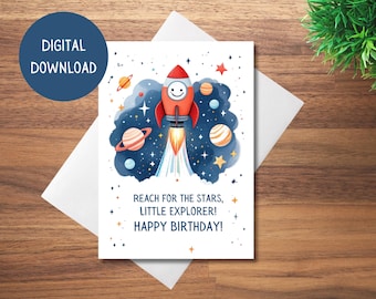 May include: A printable birthday card featuring a red rocket ship flying through space with planets and stars. The text reads "Reach for the stars, little explorer! Happy birthday!"