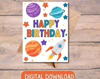 May include: A white card with a colorful "Happy Birthday" message surrounded by planets, stars, and a rocket ship. The card has a white background with colorful planets, stars, and a rocket ship.