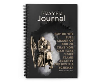May include: A black prayer journal with a spiral binding. The cover features a knight in armour kneeling in prayer with a shield and sword. The text on the cover reads "Prayer Journal" and "Put on the full armour of God so that you can take your stand against the devil's schemes Ephesians 6:11".
